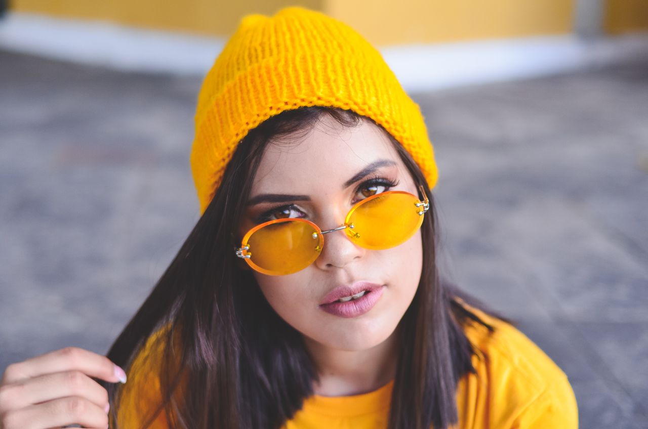 services-01 Fashionable woman wearing yellow sunglasses and hat poses confidently outdoors.