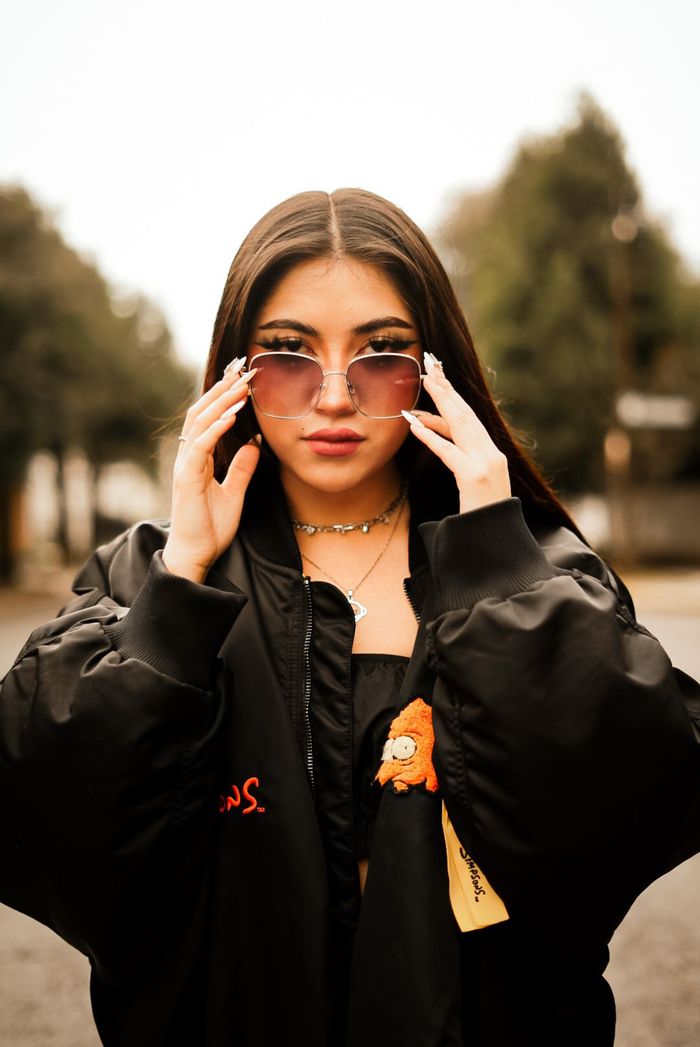 about-02 Fashionable young woman wearing sunglasses posing confidently outdoors.