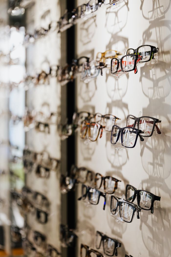 why-choose-us A variety of eyeglasses frames displayed on a wall in an optical store.